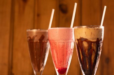 Tahta zemin üzerinde üç bardak çeşitli milkshake (çikolata, çilek ve vanilya).