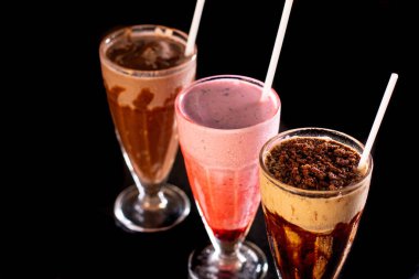 Tahta zemin üzerinde üç bardak çeşitli milkshake (çikolata, çilek ve vanilya).