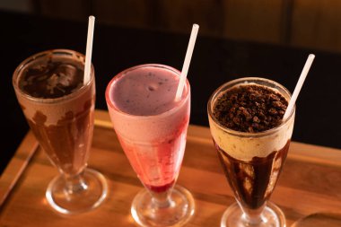 Tahta zemin üzerinde üç bardak çeşitli milkshake (çikolata, çilek ve vanilya).