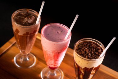 Tahta zemin üzerinde üç bardak çeşitli milkshake (çikolata, çilek ve vanilya).