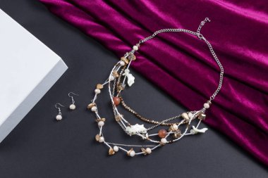 Küpe seti ve çok katmanlı kristal boncuk kolye taşlı ve deniz kabuklu gümüş zincir boho tarzı kırmızı saten atkı ve siyah kağıt arka plan.