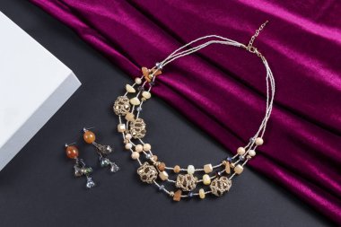 Küpe seti ve çok katmanlı tohum taneleri kristal boncuklar kolye taşlı ve altın zincirli boho tarzı kırmızı saten atkı ve siyah kağıt arka plan