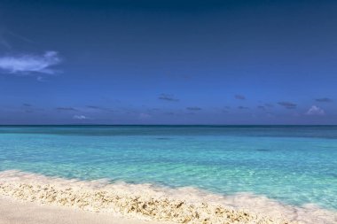 Altın sarı kum parlak güneşli bir günde mavi deniz kenarında ıssız bir sahilde.