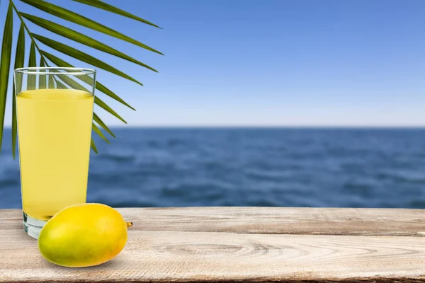 Mango i sok z mango stoją na stole naprzeciw morza. — Zdjęcie stockowe