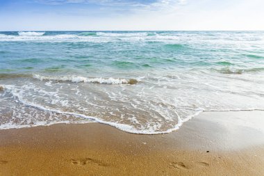 Kumlu sahilde oturan ve koyu mavi Akdeniz 'e bakan bir kız..