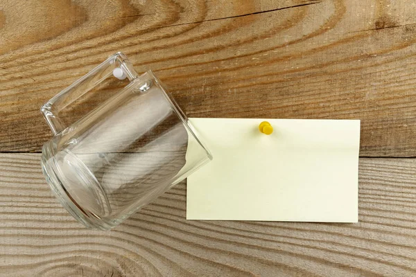 En glasmugg hänger på en spik bredvid ett papper för att skriva text. Allt på bakgrunden av en naturlig träskiva. — Stockfoto