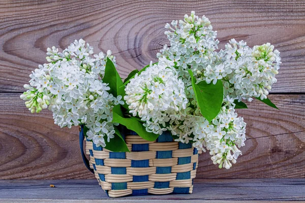 Basket with a branch of lilac flower on a wooden background. — Stock Photo, Image