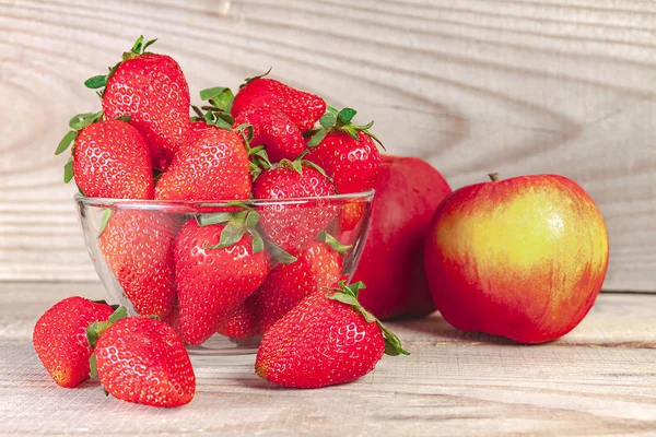 Erdbeeren in einem Glasteller mit einem Apfel auf einem hölzernen Hintergrund. — Stockfoto