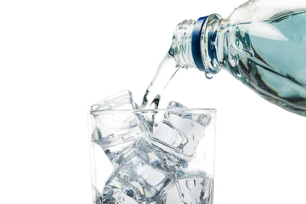 Vanuit de fles giet water in een glas ijs, op een witte achtergrond. — Stockfoto