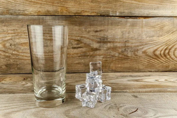 Vidrio vacío con cubitos de hielo sobre fondo de madera . — Foto de Stock