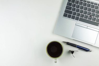 Laptop klavyesi bir kahve fincanı, bir kalem ve bir atacın yanında.