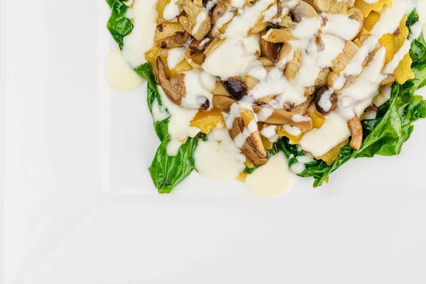 Taze kavrulmuş mantar ve kremsi parmesan peynir soslu ıspanak üzerinde beyaz plaka ile dekore edilmiş İtalyan Mantısı.