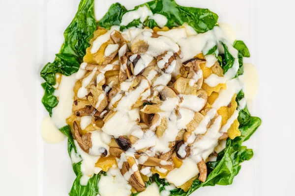 Taze kavrulmuş mantar ve kremsi parmesan peynir soslu ıspanak üzerinde beyaz plaka ile dekore edilmiş İtalyan Mantısı.