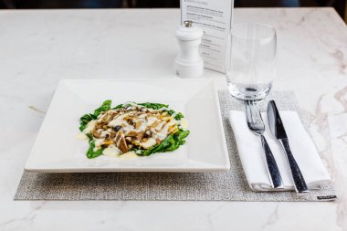 Taze kavrulmuş mantar ve kremsi parmesan peynir soslu ıspanak üzerinde beyaz plaka ile dekore edilmiş İtalyan Mantısı.