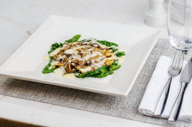 Taze kavrulmuş mantar ve kremsi parmesan peynir soslu ıspanak üzerinde beyaz plaka ile dekore edilmiş İtalyan Mantısı.