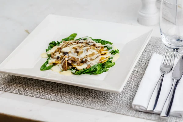 Taze kavrulmuş mantar ve kremsi parmesan peynir soslu ıspanak üzerinde beyaz plaka ile dekore edilmiş İtalyan Mantısı.