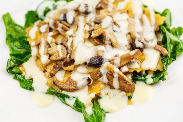 Taze kavrulmuş mantar ve kremsi parmesan peynir soslu ıspanak üzerinde beyaz plaka ile dekore edilmiş İtalyan Mantısı.