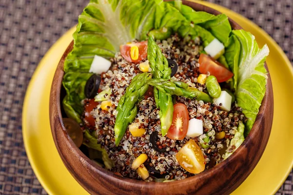 Quinoa salad with sweet corn, olive, tomato, cucumber and chives in wooden bowl