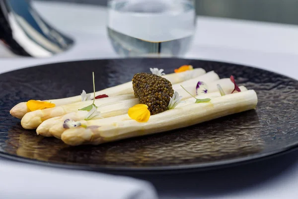 Siyah plaka üzerinde çiçeklerle dekore edilmiş havyar ile beyaz kuşkonmaz servis.