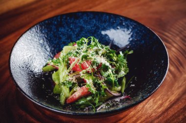 Koyu kasede servis edilen yeşil salata, ahşap arka plan.