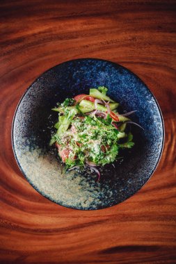 Koyu kasede servis edilen yeşil salata, ahşap arka plan.