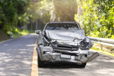 Önünde büyük hasarlı ve kaza sonucu kırılan gri renkli otomobil ilerler ve yol park yerinde artık araba kullanamaz. Metin veya tasarım için kopyalama alanı ile