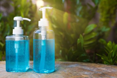 Bulanık yeşil arka plan ve güneş ışınları üzerine mavi alkollü jel şişesi. Pompa şişesinde el dezenfektanı. Metin veya tasarım için kopyalama alanı ile birlikte. Ahşap masada mavi alkollü jöle. İki farklı boyutta pompa şişesinde alkol jeli.. 