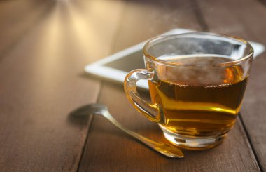 Sıcak çay fincanını çay kaşığı ve tablet iğnesiyle güneş ışınları arkaplanırken kapat. Nazikçe odaklan ve çay bardağına odaklan. metin veya tasarım için kopyalama alanı olan bardakta sıcak çay.