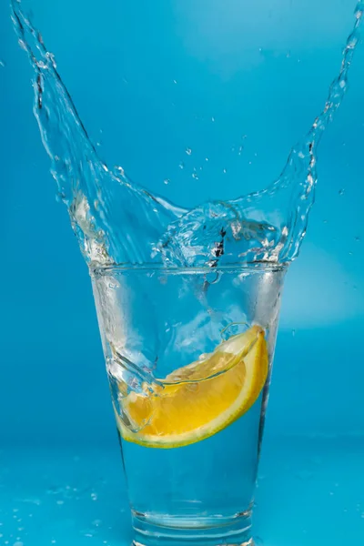 Fetta Limone Che Cade Cade Bicchiere Spruzzante Con Sfondo Azzurro — Foto Stock