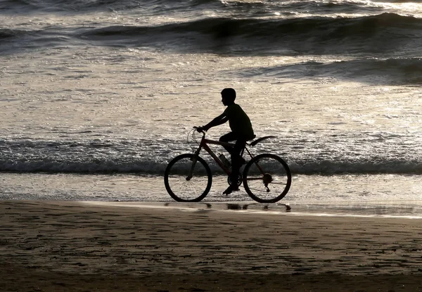 Silhouette of a boy riding a bike along the ocean after sunset