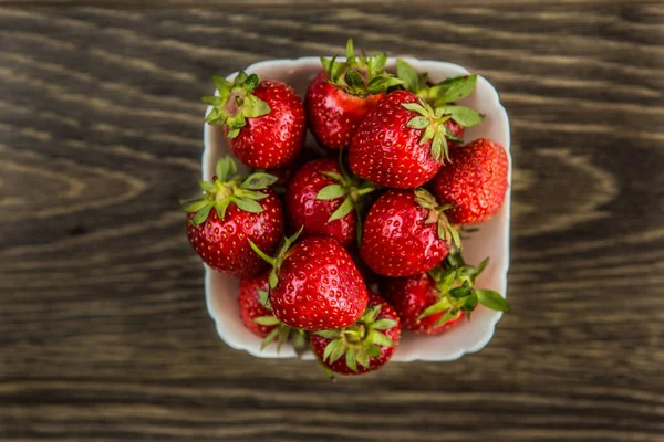 Bir küçük beyaz porselen kase sulu taze olgun kırmızı çilek ile dolu. Dokulu masa üstü. Taze çilek. Bir kase çilek