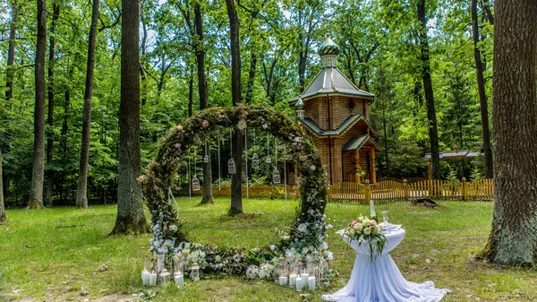 Arch for the wedding ceremony. Decorated with fabric flowers and greenery. Is located in a pine forest. Background church. Candles in decorated jars. Just married. Wedding decor. — Stock Photo, Image