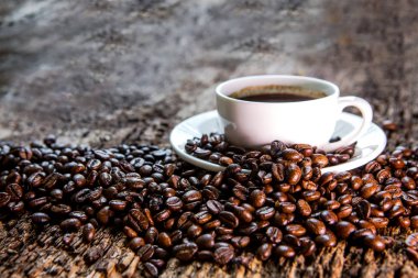 Sıcak kahve Kupası ve kızartma kahve çekirdekleri ahşap bir masa üzerinde. Koyu arka plan