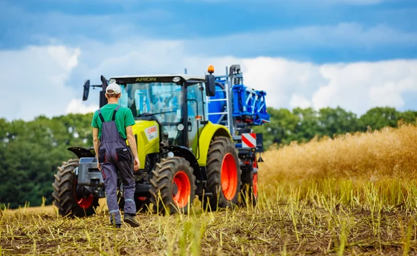 Vinnytsa，乌克兰-7 月 2017年: 站在农田上英俊的年轻农民。拖拉机在后台工作 — 图库照片
