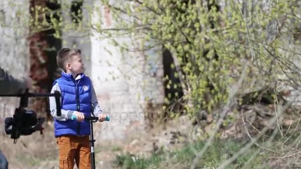 Pojke skridskor på en skoter bland ruinerna — Stockvideo