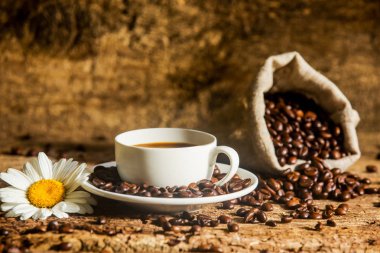 Kahve fincanı ve ahşap arka plan üzerinde güzel beyaz çiçekli ahşap bir masa üzerinde kızarmış kahve çekirdekleri