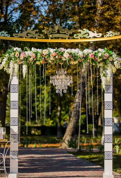 Arch til bryllupsceremonien. Dekoreret med krystal lysekrone og friske blomster. Bryllupsdekorationer. De nygifte . - Stock-foto