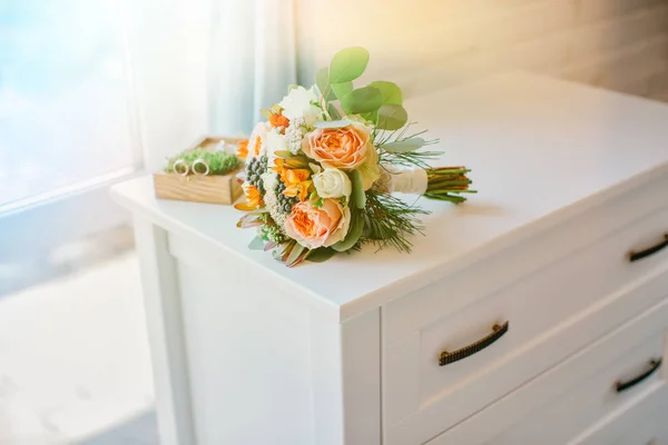 Bridal bouquet of white and orange flowers on a white table. Wedding accessories of the bride