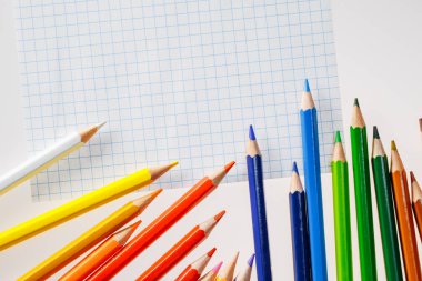 Beyaz arka plan üzerinde renkli kalemler. Metin için özgür yer. Çizim, eğitim, okul, yaratıcılık için araçları. Masanın üstünde belgili tanımlık defter yaprağının.