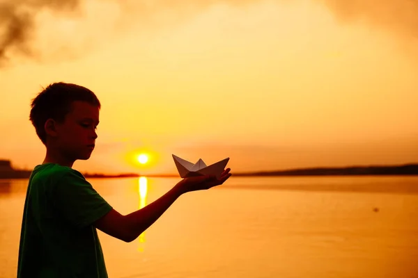 Kleine Jungen starten Papierboote am Strand im Sommer. schöner Sonnenuntergang. Origami. Fluss. See. — Stockfoto