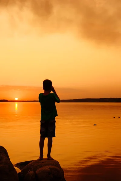 Mały chłopiec uruchomienie papieru statków z riverside. Pływające statki na odległość. Piękny zachód słońca. Origami. Rzeka. Jezioro. — Zdjęcie stockowe