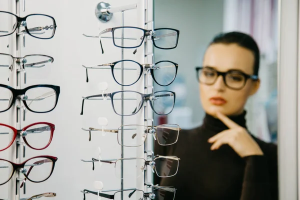 Stå med glasögon i butiken av optik. Vacker flicka i glasögon på en bakgrund. Selektivt fokus — Stockfoto