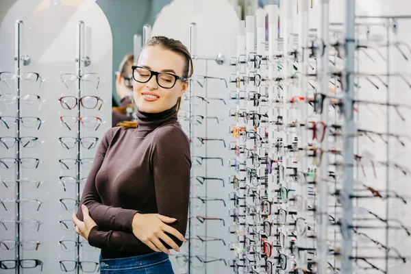 Oftalmología. Mujer joven está eligiendo unas gafas en la tienda de óptica. Corrección de la vista . — Foto de Stock