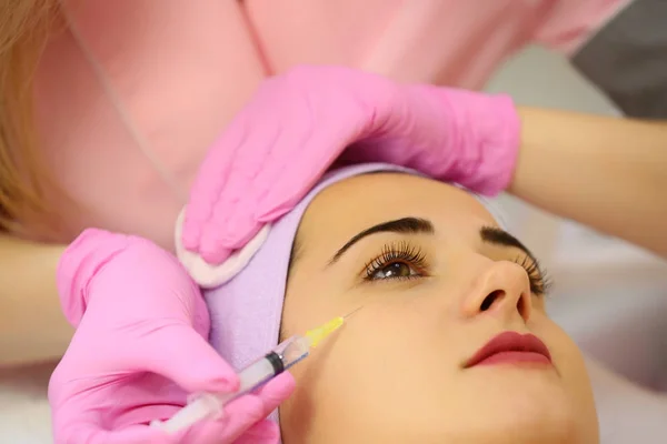 Woman receiving a botox injection in the eye zone lying in bathrobe on the medical couch — Stock Photo, Image