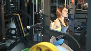 Fitness salonunda egzersiz. Genç atletik kadın güç egzersizleri bacaklar için gerçekleştirir. Simülatörü Smith