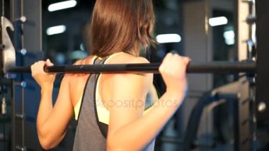 Arkadan görünüş güçlü bir genç kadının modern bir spor salonu olarak yoğun bir çalışma sırasında mekik yapıyor. Yakın çekim.