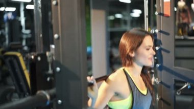 Genç güzel kız kalça ve bacak kaslarının iyileştirilmesi üzerinde bir halter ile ağız kavgası yapıyor bir spor salonunda.