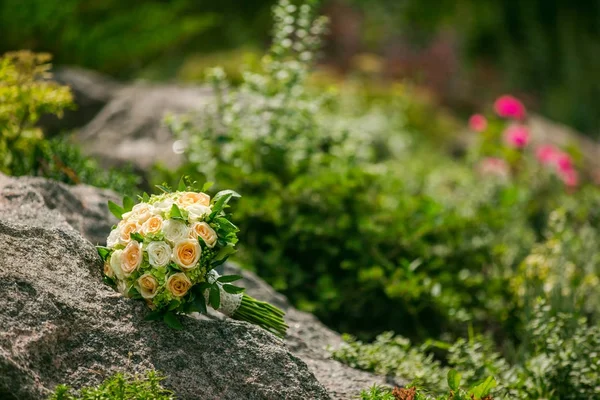 Γαμήλια ανθοδέσμη από λουλούδια και την πρασινάδα με κορδέλα βρίσκεται πάνω σε ένα βράχο σε ένα υπόβαθρο της πρασινάδας. Διακοσμήσεις γάμου. — Φωτογραφία Αρχείου