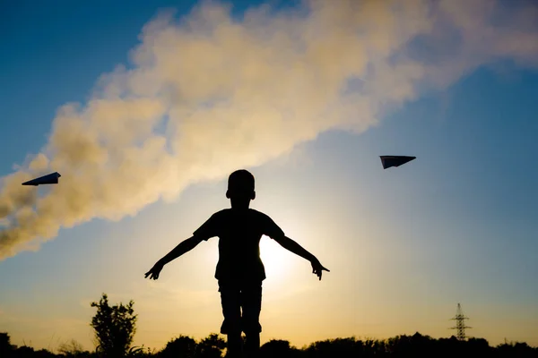 Силуэт мальчика, бросающего бумажный самолет на фоне дымящейся трубки. Экология . — стоковое фото