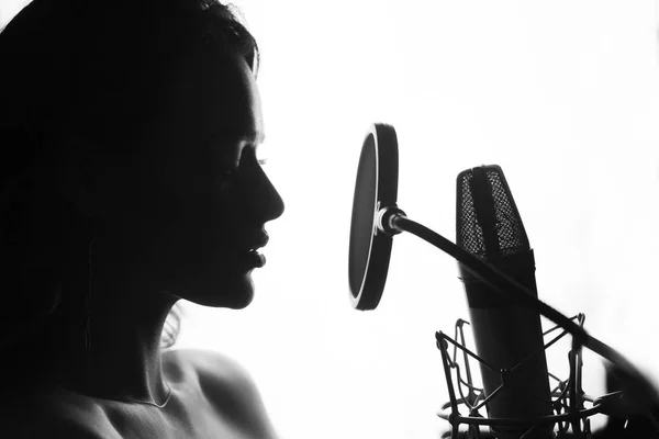 Mujer cantando en el estudio de grabación. Perfil de una mujer con una cara y labios hermosos. Blanco y negro — Foto de Stock